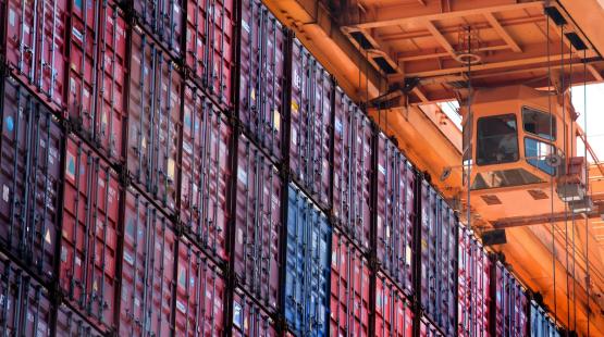 Rows of stacked red shipping containers viewed from below with an orange crane and operator cabin overheard
