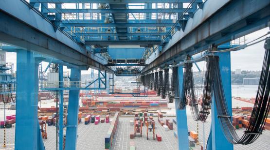 A large blue gantry crane over a shipping yard with rows of cargo containers.