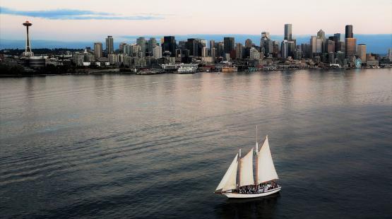 The Bay Lady sailboat moves across calm water with a city skyline in the background.