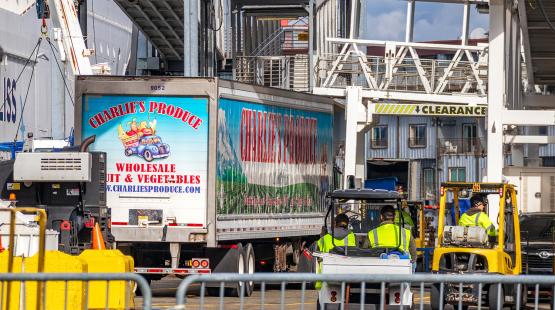 Charlie’s Produce truck being loaded at a port facility, with workers in high‑visibility clothing and equipment nearby.
