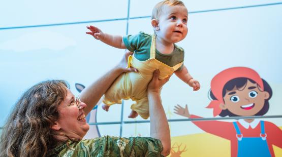 Infant is held up by parent and holds out their arms like they are flying.