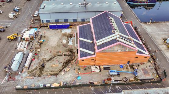 Aerial view of a construction site with an unfinished building surrounded by equipment, materials, and fenced-off work areas.