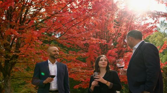 Three people wine tasting with a backdrop of fall foliage.