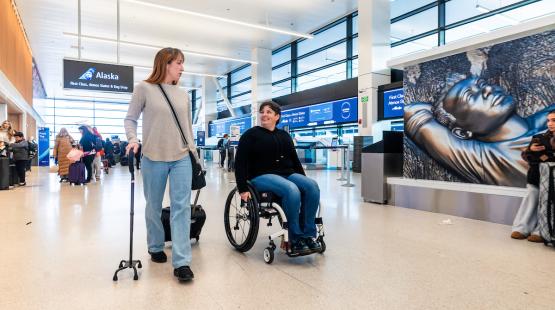 Traveler in a wheelchair and traveler with a cane walking down ticketing