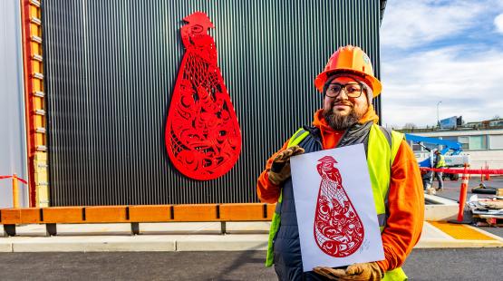 Ty Juvinel poses in the foreground with his piece "Beach Seining" on the Maritime Innovation Center building.