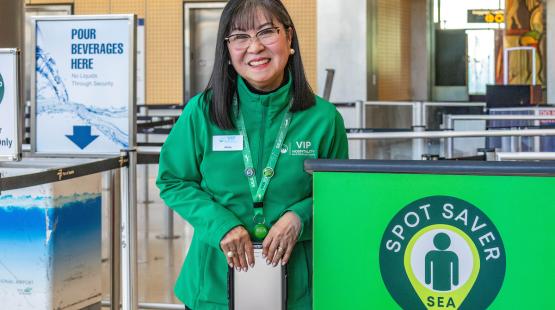 SEA Spot Saver employee is wearing a green jacket and smiling by the Spot Saver podium