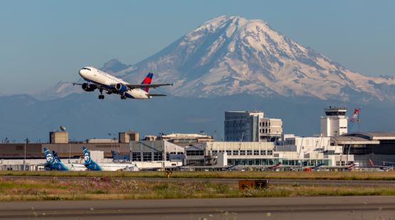 A commercial jet takes off from SEA Airport, with Mt. Rainier in the background