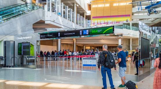 Two travelers walk towards Checkpoint 1, one with roller bag carry-on
