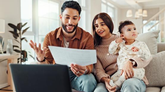 Parents discuss a document over an open laptop while mom holds baby